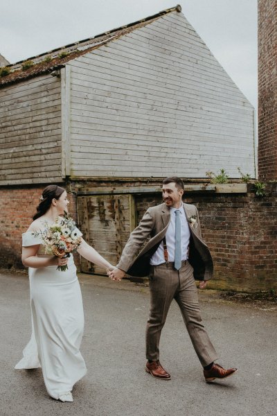 Bride and groom walk hand in hand carrying bouquet flowers