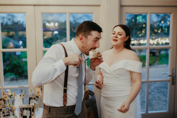 Bride and groom with piece of cake beside window