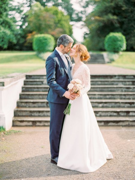 Bride holding Pink white roses flowers bouquet groom kiss steps in background