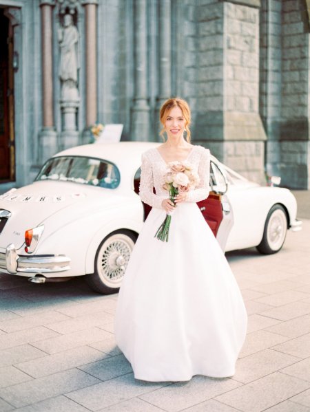 Bride outside of church beside wedding car