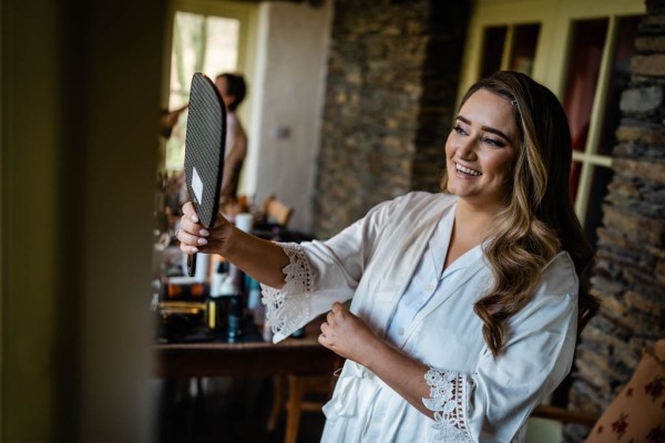 Bride wearing robe looking in mirror at makeup