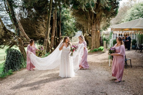 Bride and bridesmaids pink dresses outside holding bouquet of flowers holding veil