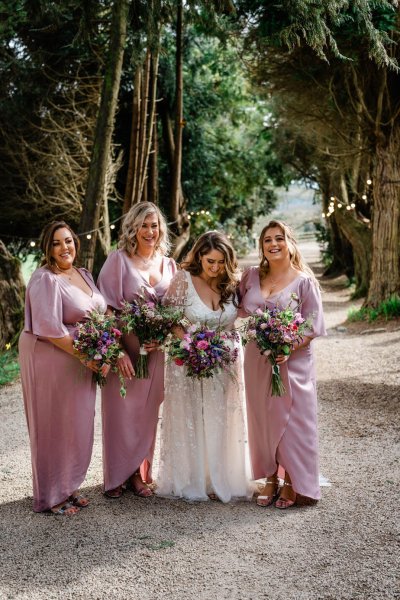 Bride and bridesmaids pink dresses outside holding bouquet of flowers