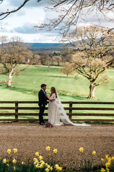 Bride and groom farm at fence green landscape trees