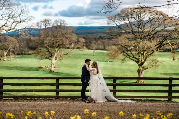 Bride and groom farm at fence green landscape trees