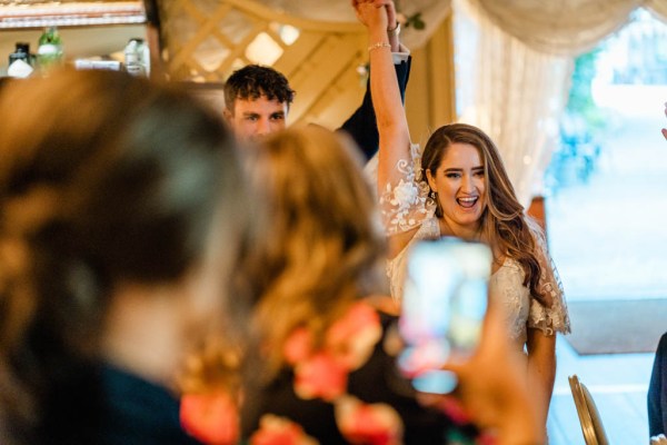 Bride and groom enter tent holding hands hand in the air