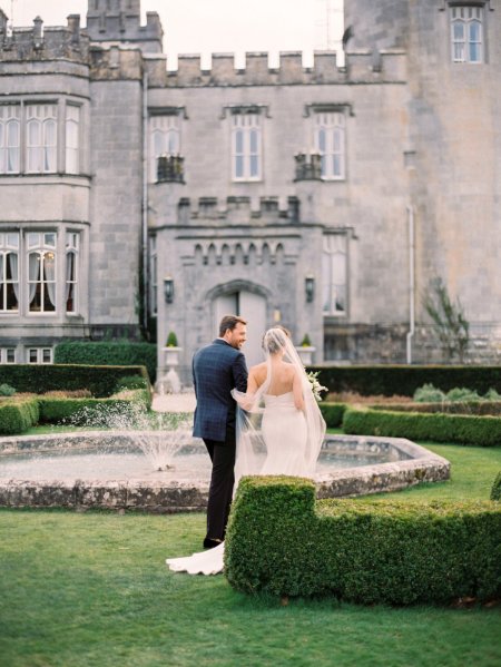 Dromoland Castle in background bride and groom walk around garden