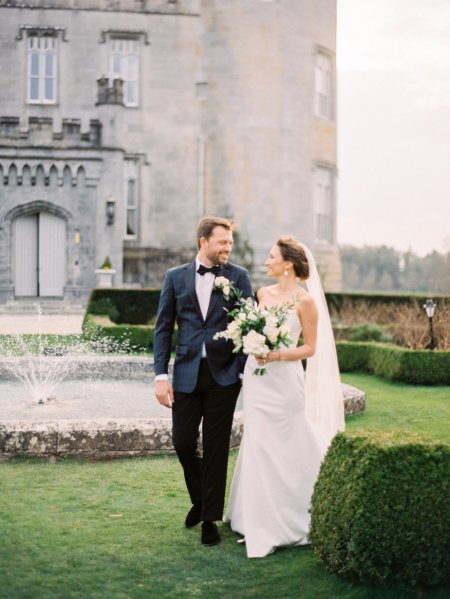 Dromoland Castle in background bride and groom walk around garden