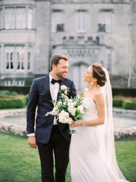 Dromoland Castle in background bride and groom walk around garden bouquet of flowers