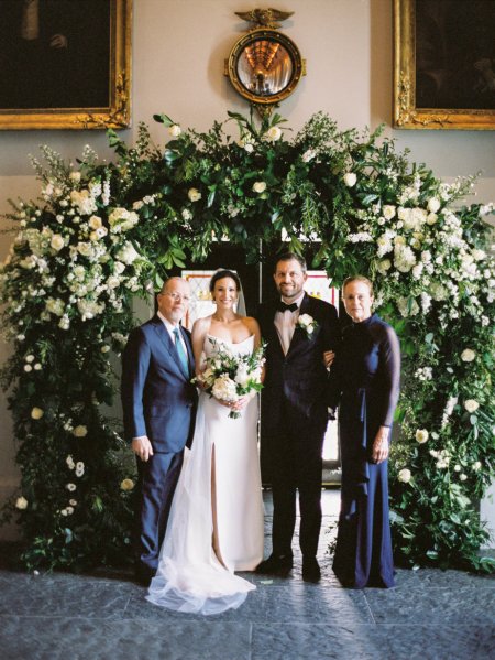 Bride and groom under bed of flowers during wedding ceremony bouquet family mother father