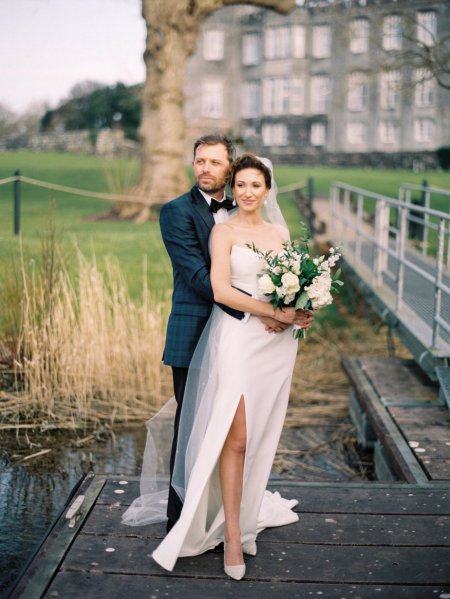 Bride and groom look over lake holding bouquet