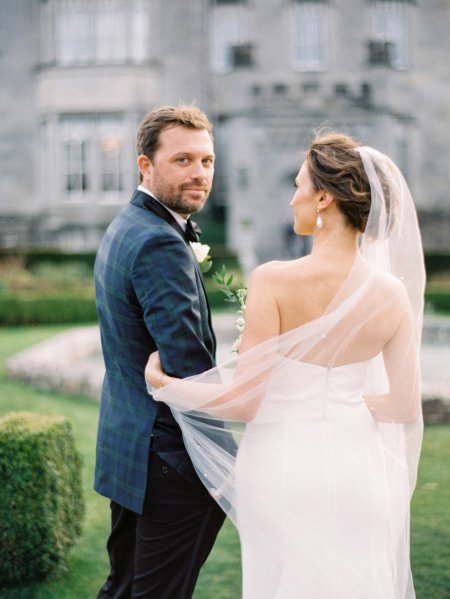 Groom looks over his shoulder arm in arm with bride