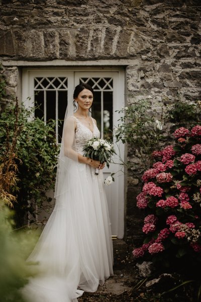 Bride on her own beside a wall of flowers