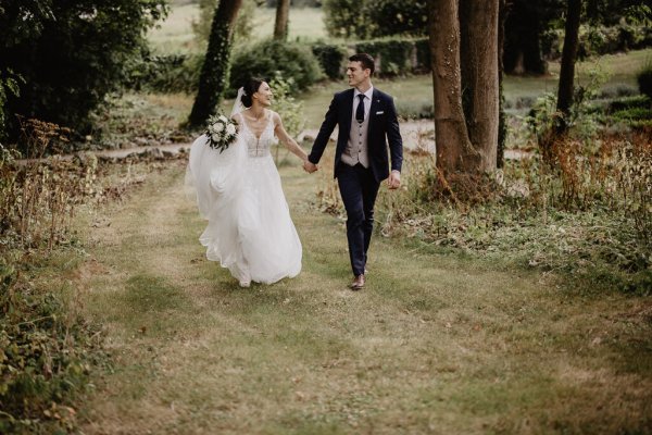 Bride and groom walk through park on grass