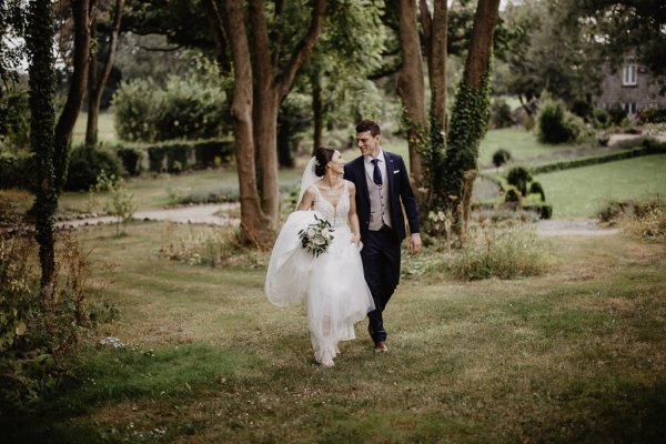 Bride and groom walk through park on grass