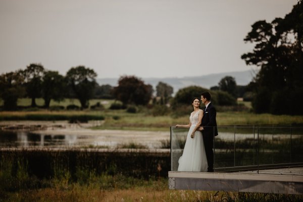 Bride and groom overlook lake on boardwalk Ferris wheel in background