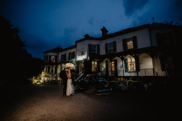 Bride and groom holding umbrella outside wedding venue