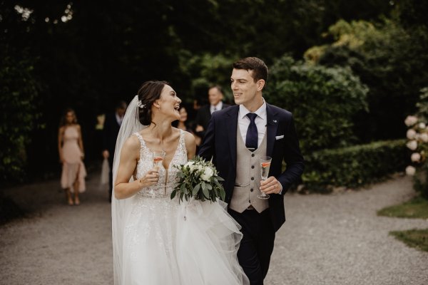 Bride and groom holding champagne walking