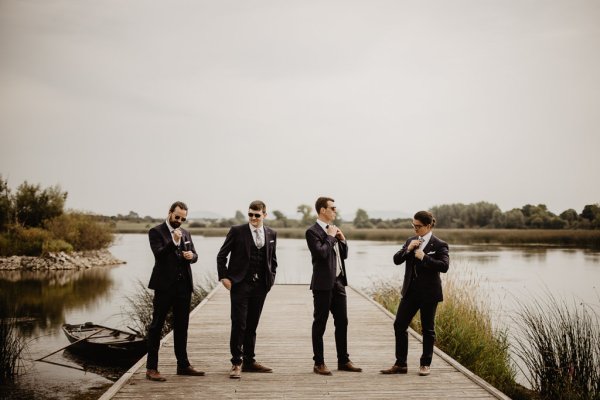 Groom and groomsmen on boardwalk beside lake wearing sunglasses