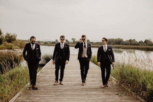 Groom and groomsmen on boardwalk beside lake