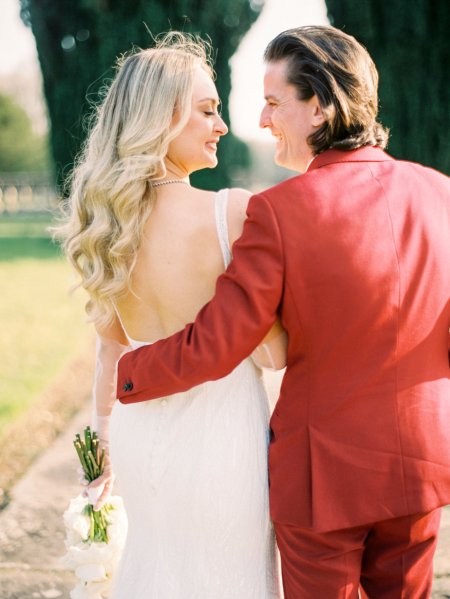 Bride and groom red suit white dress flowers exterior from behind