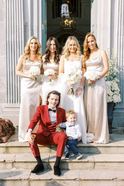 Bride bridesmaids groom and little boy sit on step outside venue