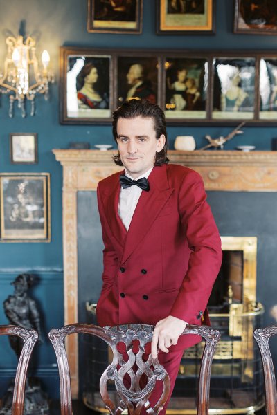 Groom wearing red suit interior manor house bow tie