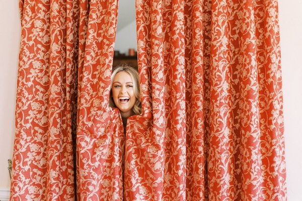 first look with bridesmaids Bride pops her head out of red curtains