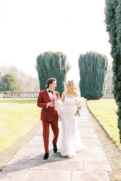 Bride and groom walking towards stately home manor wedding venue flowers and champagne