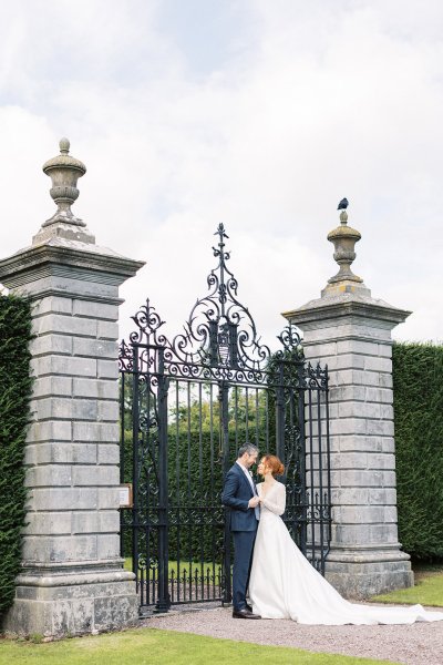 Bride and groom stand facing camera in front of pillar entrance