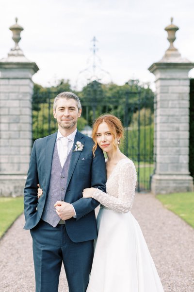 Bride and groom stand facing camera in front of pillar entrance