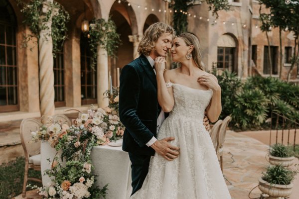 Muted Rainbow Styled Shoot couple holding bouquet of flowers on table dining exterior candles over the shoulder embrace