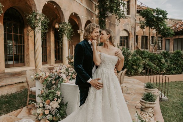 Muted Rainbow Styled Shoot couple holding bouquet of flowers on table dining exterior candles over the shoulder embrace