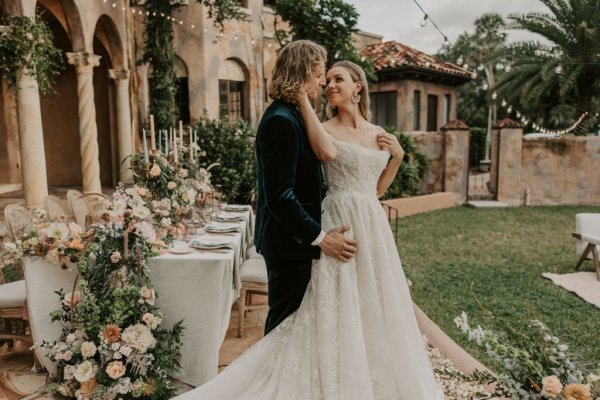 Muted Rainbow Styled Shoot couple holding bouquet of flowers on table dining exterior candles