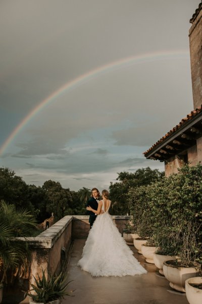 Muted Rainbow Styled Shoot couple holding bouquet of flowers scenic background rainbow above