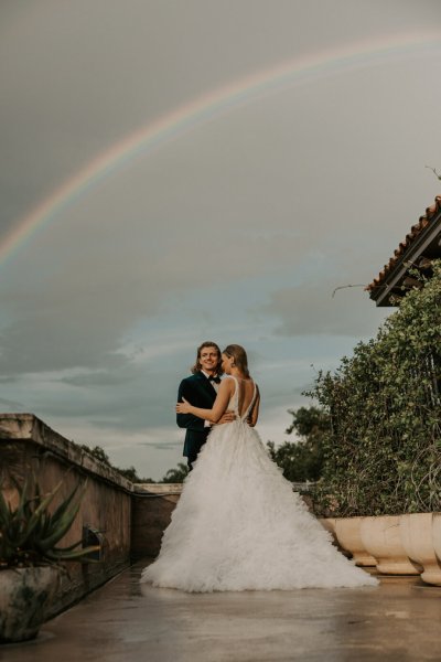 Muted Rainbow Styled Shoot couple holding bouquet of flowers scenic background rainbow above