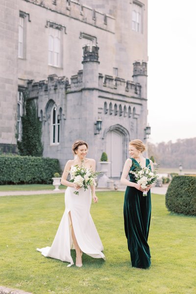 Mother of the bride wearing dark green silky gown on grass holding bouquet and flowers