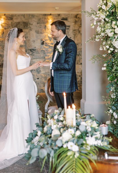 Bride and groom during vows holding hands candles lighting on table with flowers