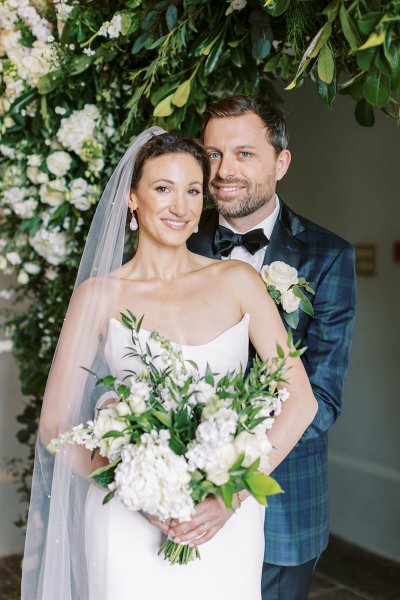 Bride and groom look towards camera holding bouquet of flowers white