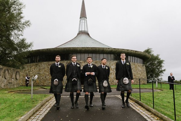 Groomsmen and groom wearing kilts and bagpipes outside of venue church