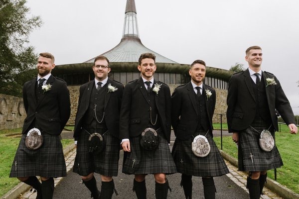 Groomsmen and groom wearing kilts and bagpipes outside of venue church