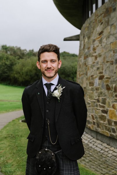 Groom wearing kilt and bagpipe outside of venue church