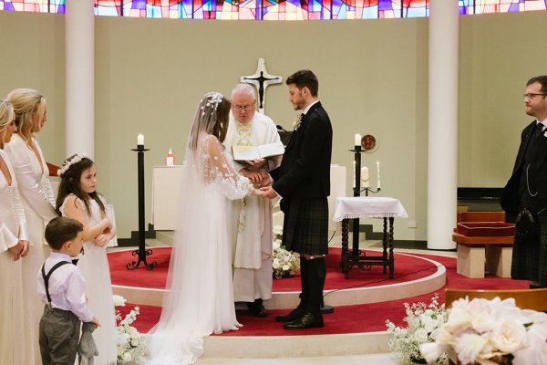 Bride and groom stand at alter with priest during church ceremony