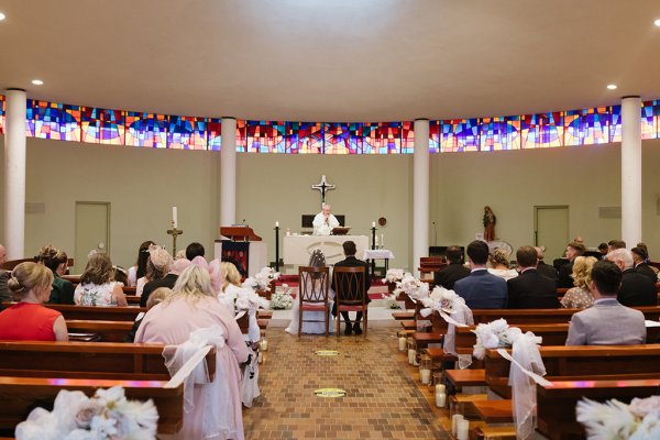 Bride and groom sitting beside alter priest church ceremony