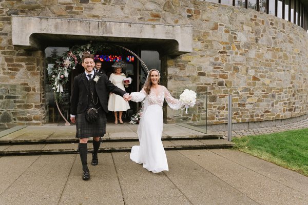 Bride and groom exit church carrying white roses flowers