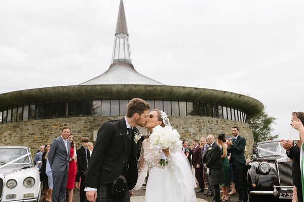 Bride and groom church in background as well as guests