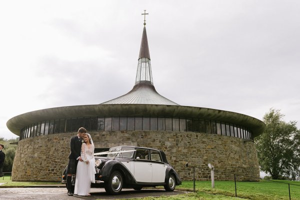 Bride groom outside of church standing beside wedding car