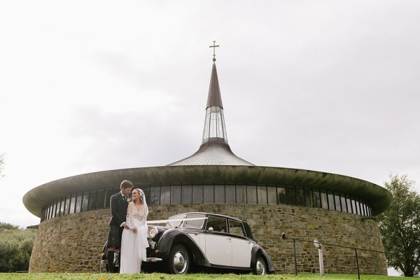 Bride groom outside of church standing beside wedding car