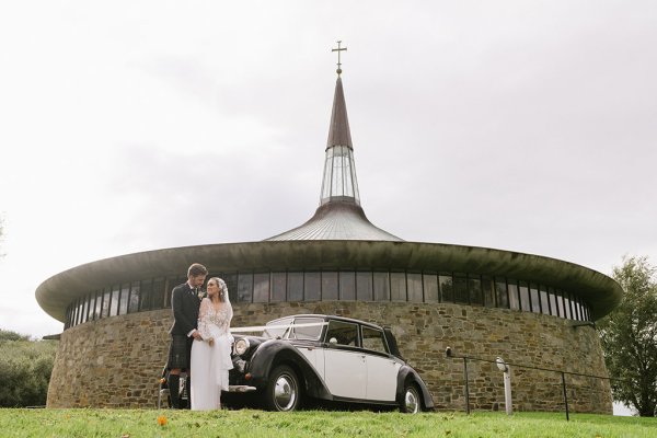 Bride groom outside of church standing beside wedding car