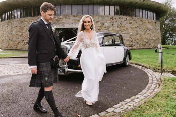 Bride and groom walking in front of wedding car